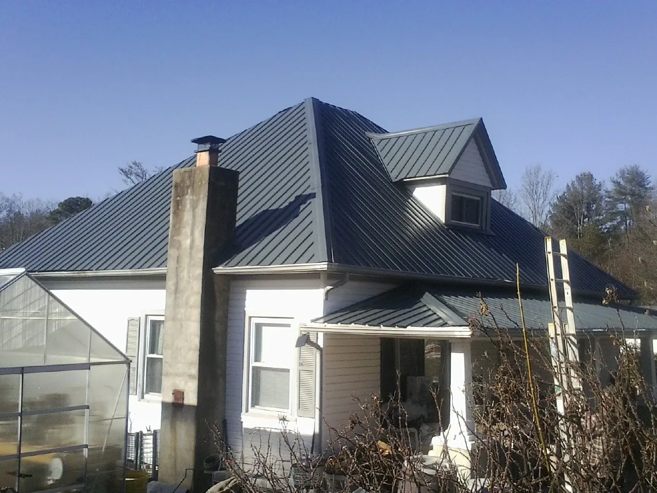 Dark blue standing seam metal roof on a white farmhouse with dormer — Slate & Tile Roof Repair by Roofing Brothers in Olga
