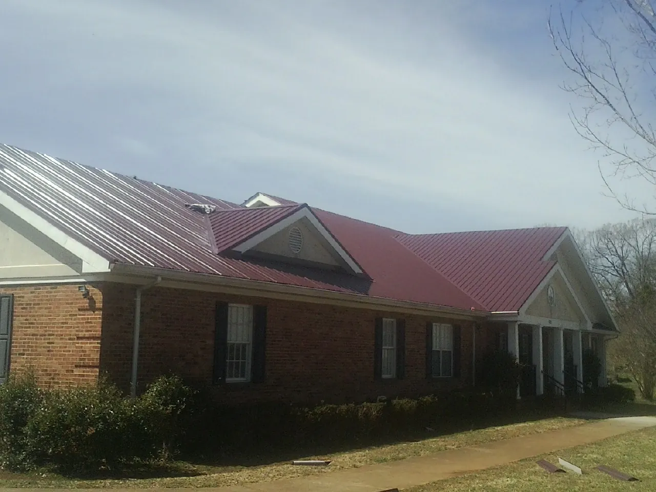 Red metal roof with gabled entries on a long brick building, from a Hail Damage Roof Repair job in Olga
