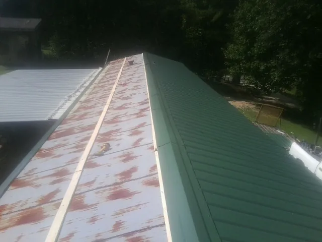 Old rusted panels beside newly installed green metal roofing — Wind Damage Roof Repair by Roofing Brothers in Olga