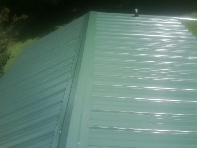 New green metal panels meeting at the ridge of a roof — Flat Roof Repair work by our crew in Olga