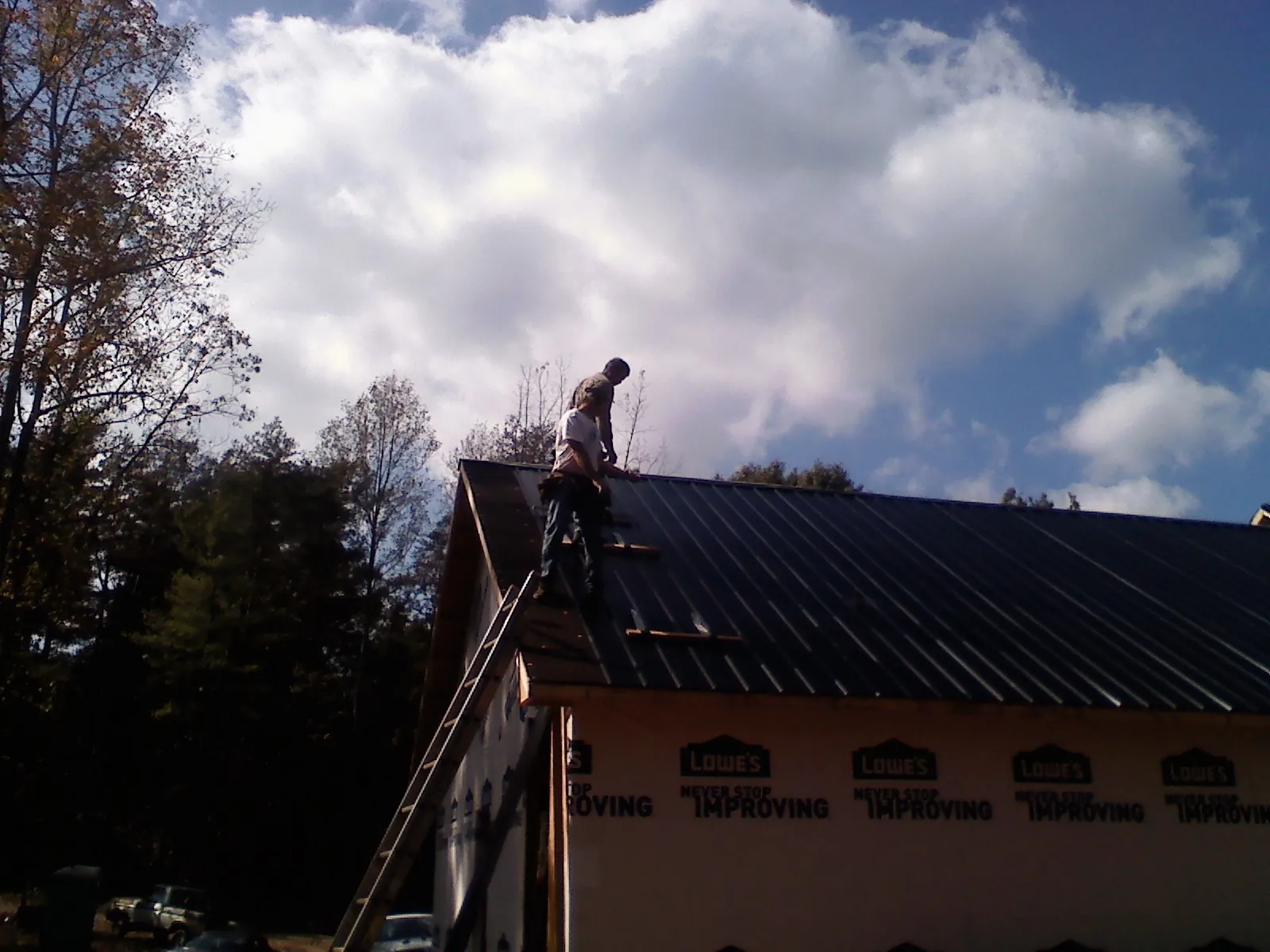 Roofer fastening dark metal panels high against a cloudy sky, from a Roof Inspection job in Olga