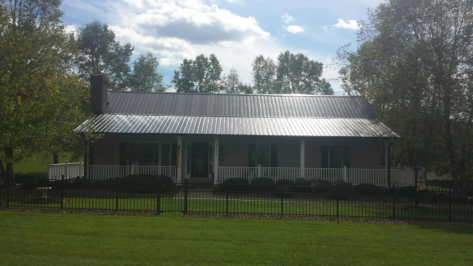Gray metal roof on a brick ranch with a full width front porch — Gutter Guard Installation work by our crew in Olga