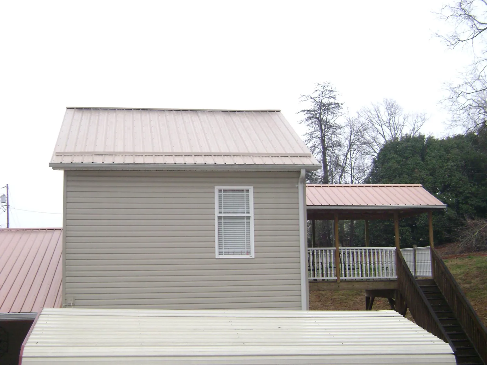 Tan metal roofs on a two story addition and attached porch, from a Roof Replacement job in Olga